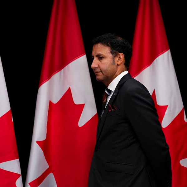 Arif Virani standing in front of Canadian flags