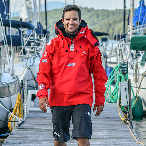 Simon DuBois smiling, walking down a dock surrounded by sailboats