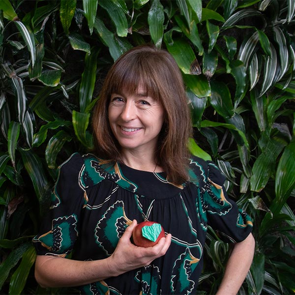 A woman holding an apple in front of a leafy wall.