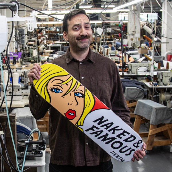 A man holding a skateboard in a manufacturing room with other people.