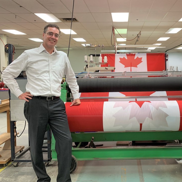 A man standing next to a machine with rolls of the Canadian flag.