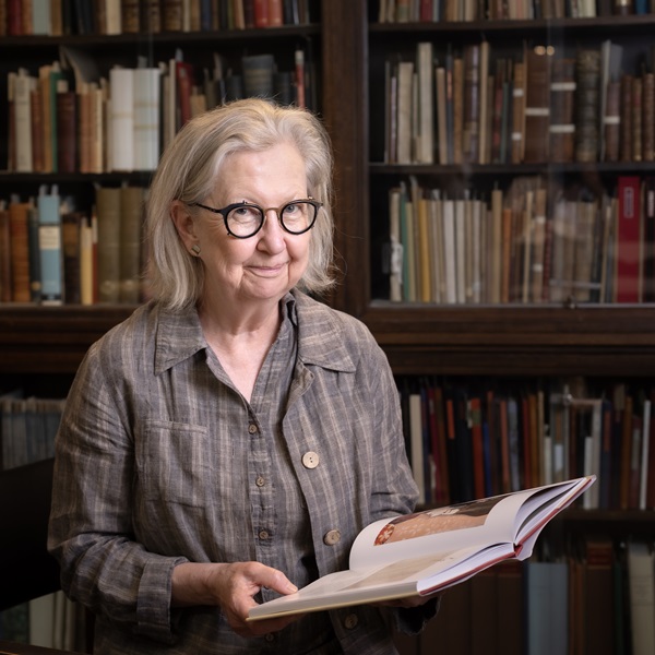 A woman holding a book in front of a bookshelf.